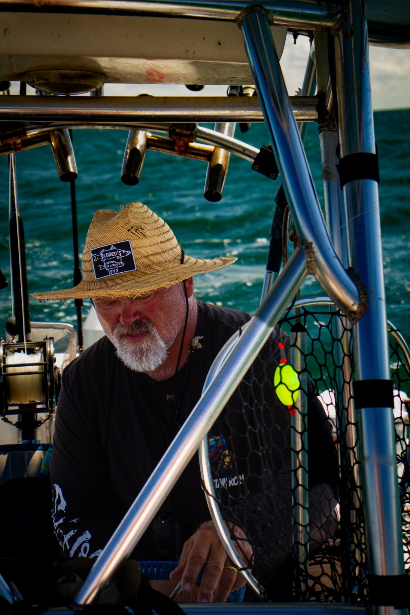 Fisherman in a straw hat working on a boat with open water behind him