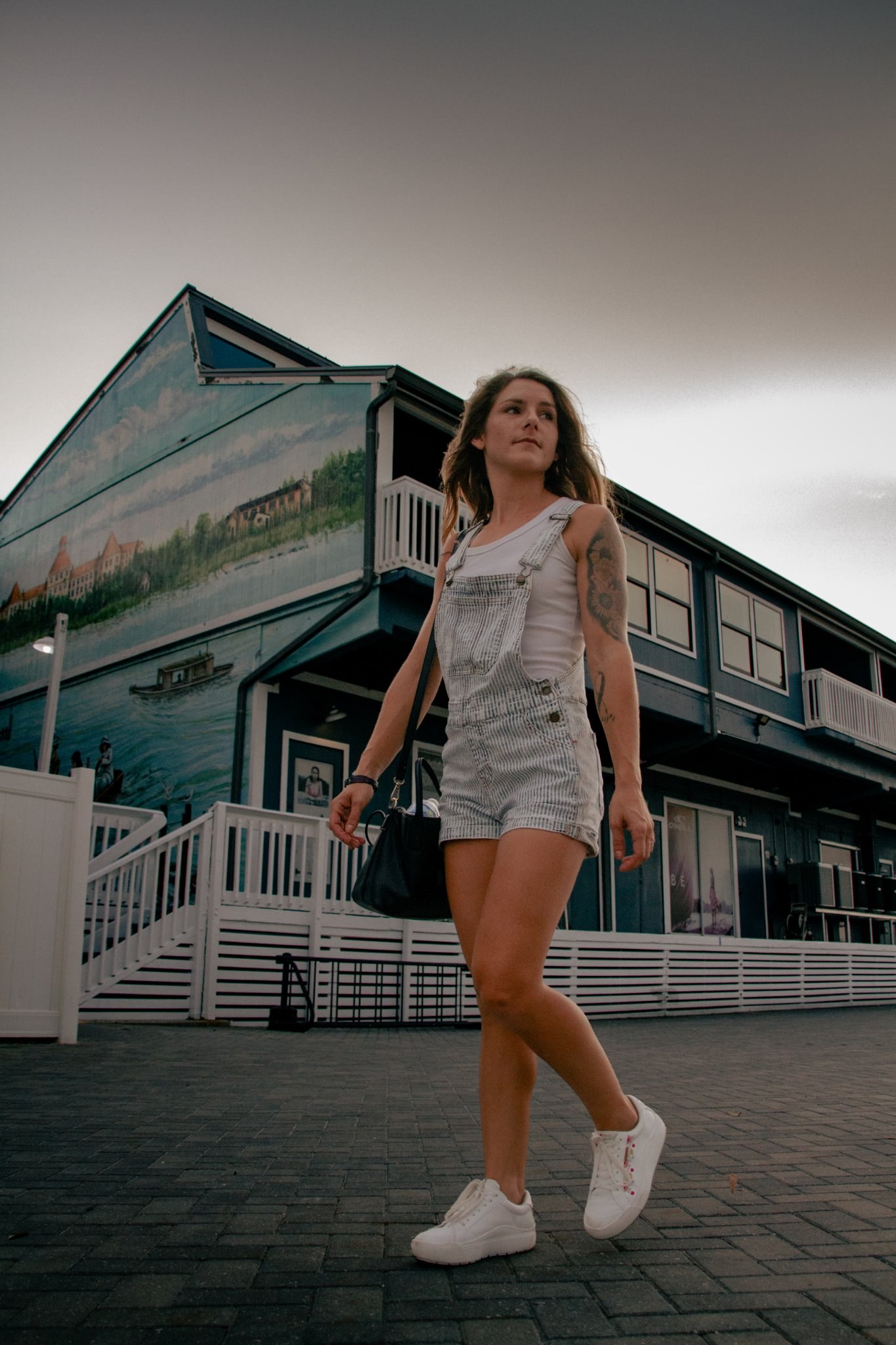Woman in overalls walking past a building with a painted mural