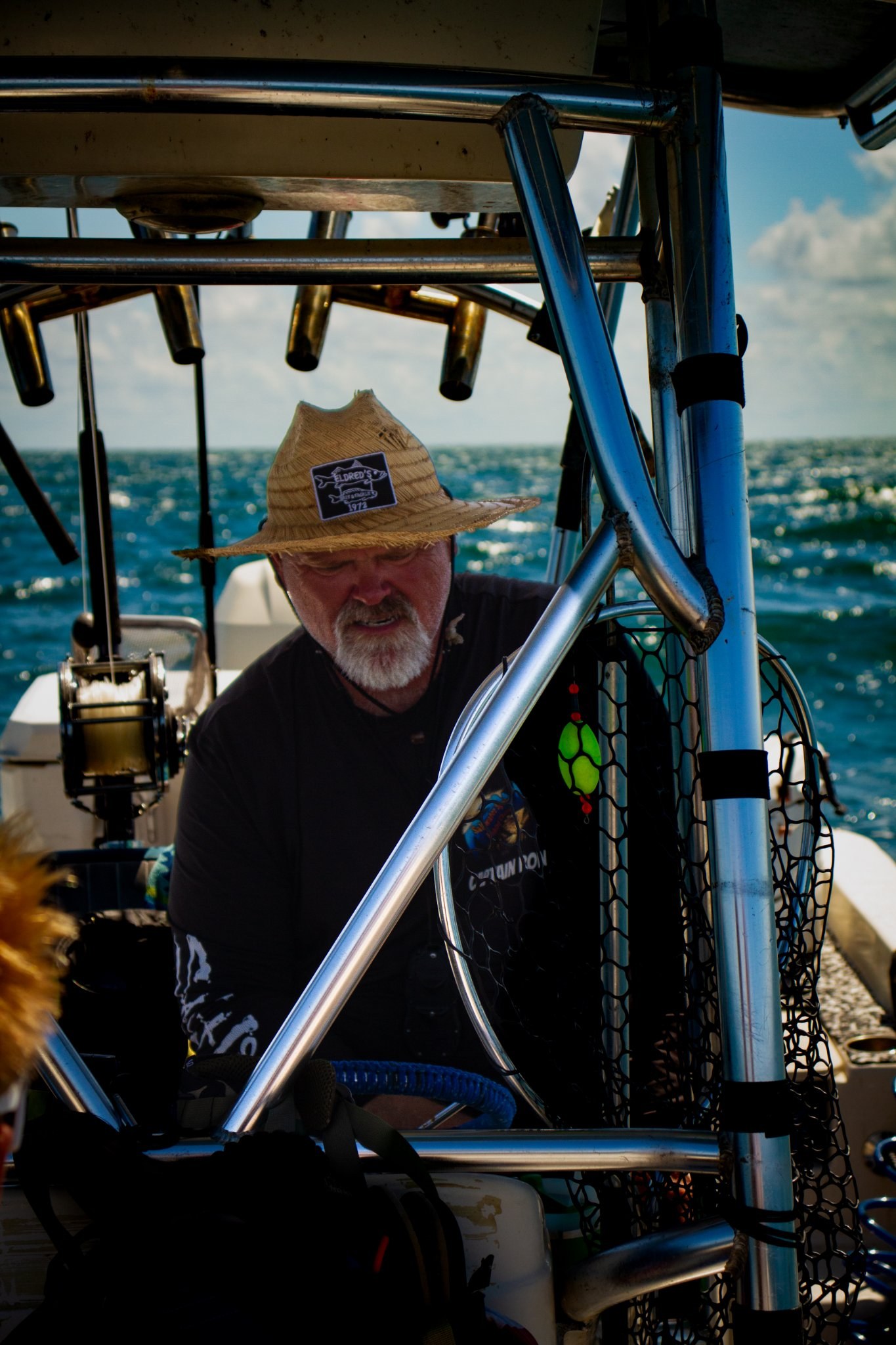 Fisherman in a straw hat on a boat, second angle, with sparkling water behind him